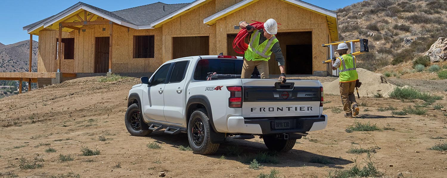 A white Nissan Frontier with a worker in the truck bed, parked in front of a house being constructed.