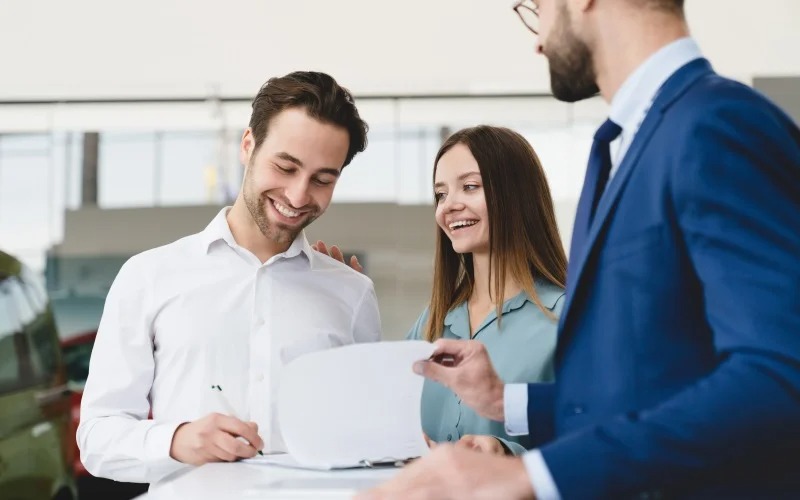 Couple in dealer showroom signing finance papers with manager